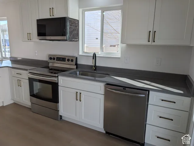 White shaker-style cabinetry with dark hardware, stainless steel appliances, dark countertops, and wood-finish flooring