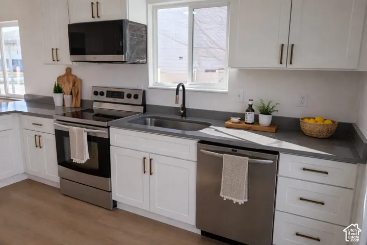 White cabinetry with dark hardware, stainless steel appliances, gray countertops, and wood-finish flooring