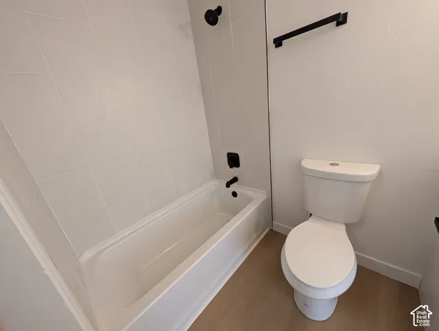 White bathtub with matte black fixtures, white tile surround, and wood-finish flooring