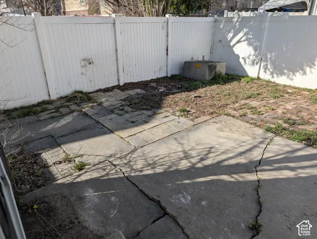 Outdoor area featuring a white privacy fence, concrete patio, and brick paving