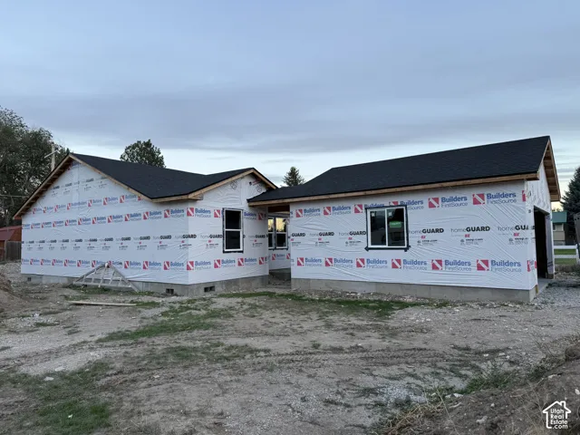 New construction exterior featuring a black shingle roof, white house wrap, and multiple windows