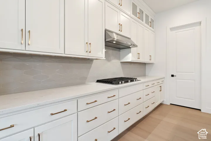 White cabinetry with bronze hardware, stainless steel range hood, hexagonal tile backsplash, quartz countertops, and wood-finish flooring