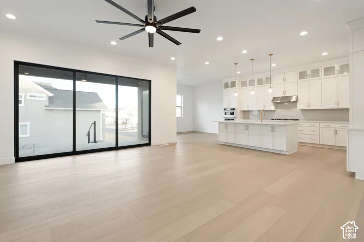 Expansive open concept interior featuring wood-finish flooring, a large kitchen island with pendant lighting, and abundant white cabinetry