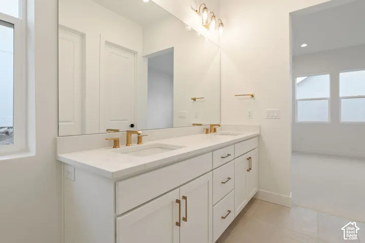 Dual vanity with integrated sinks, gold-finish fixtures, a full-width mirror, and overhead lighting