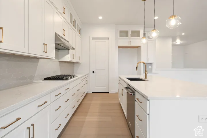 White shaker-style cabinetry with gold-tone hardware, a gas cooktop, hexagon tile backsplash, a kitchen island with a built-in sink, and pendant lighting