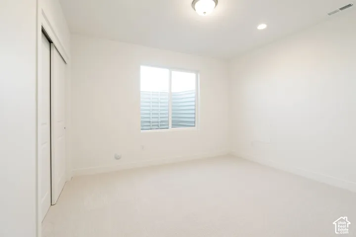 Carpeted flooring with white painted walls, a sliding two-panel closet door, and a single window with a window well