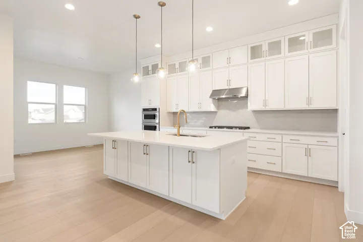 Spacious kitchen featuring an expansive island with a white countertop, white cabinetry with gold-tone hardware, stainless steel appliances, and wood-finish flooring