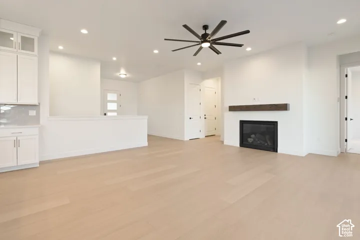 Light wood-finish flooring, built-in white cabinetry with glass inserts, recessed lighting, modern ceiling fan, and a fireplace with a wood mantel