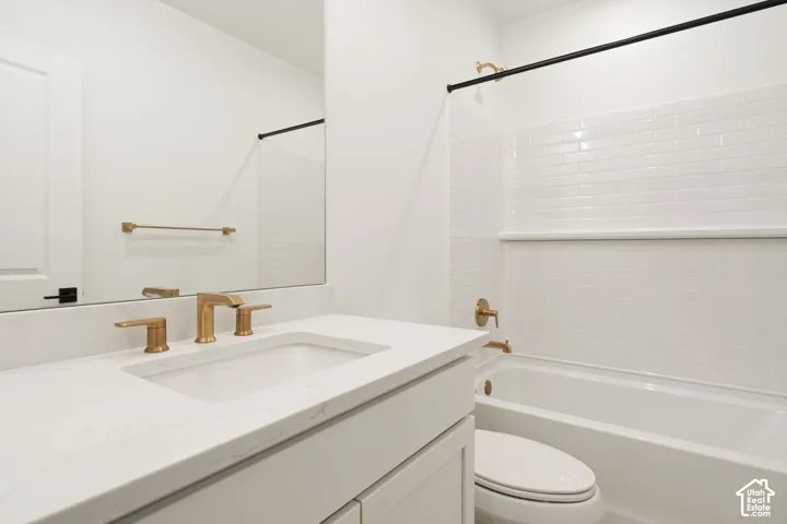 Bathroom featuring a spacious vanity with an undermount sink, brass-finish fixtures, and a subway tile bath surround