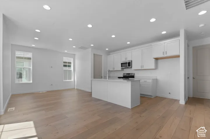 Open-concept living space featuring wood-finish flooring, recessed lighting, a kitchen island, white cabinetry, and stainless steel appliances