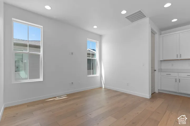 Recessed lighting, wood-finish flooring, two large windows, built-in white cabinetry, and a light-toned countertop