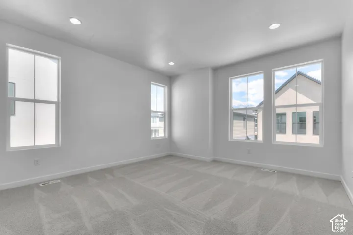Recessed ceiling lighting, multiple large windows, white baseboards, and light-toned patterned carpeting