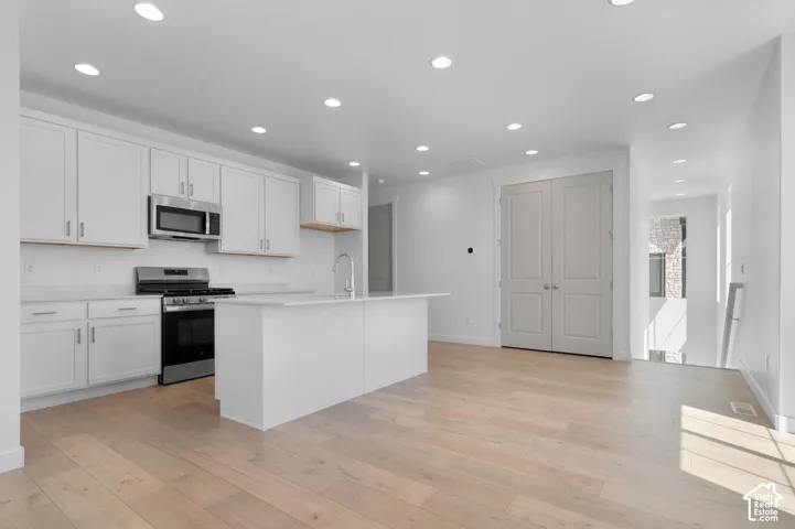 White shaker cabinetry with stainless steel appliances, a central island, recessed lighting, and light wood-finish flooring