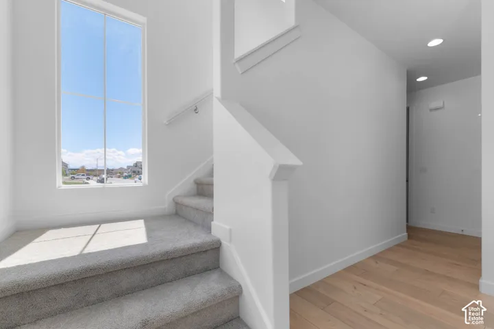 Two-story entryway featuring a tall picture window, neutral carpeting on stairs, wood-finish flooring, and recessed lighting