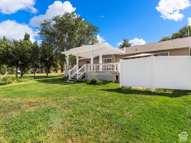 Expansive green lawn, elevated wooden deck with pergola, white vinyl fencing, and mature trees