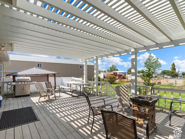 Spacious outdoor deck with a slatted pergola, white railing, and a stone-clad fire pit