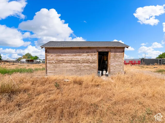 Detached wooden storage shed with an open doorway and a dark shingle roof