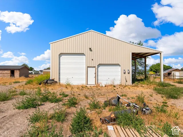 Metal-sided outbuilding featuring two garage doors, an entry door, and an attached covered extension