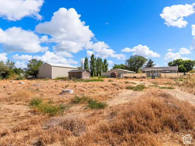 Expansive land with multiple structures including a large metal-sided building, a smaller rustic shed, and a single-story residence with a covered porch