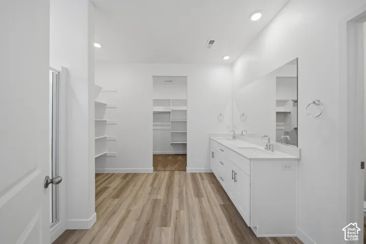 White double vanity with dual sinks, overhead recessed lighting, wood-finish flooring, and built-in shelving