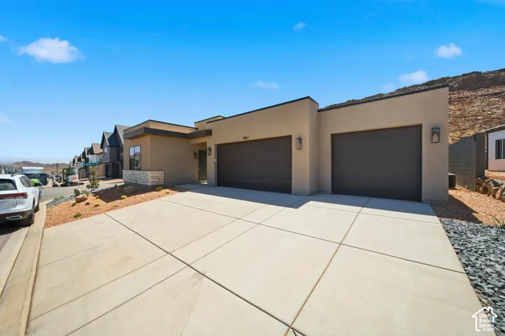 Modern stucco exterior, stone accent detailing, dual garage doors, contemporary exterior lighting, concrete driveway