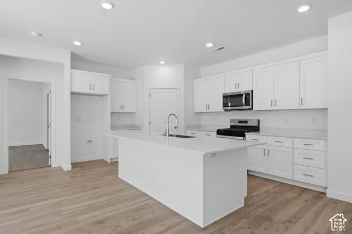 Kitchen featuring a large central island, white shaker-style cabinetry, stainless steel appliances, and light-toned wood-finish flooring