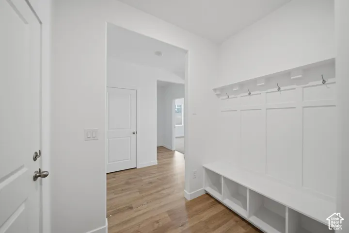 Entryway featuring wood-finish flooring, white paneled walls, a built-in bench with cubby storage, and wall-mounted coat hooks