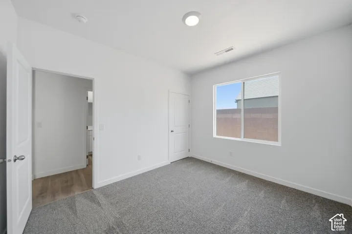 Spacious room featuring gray carpeting, white walls, and a large window with blinds