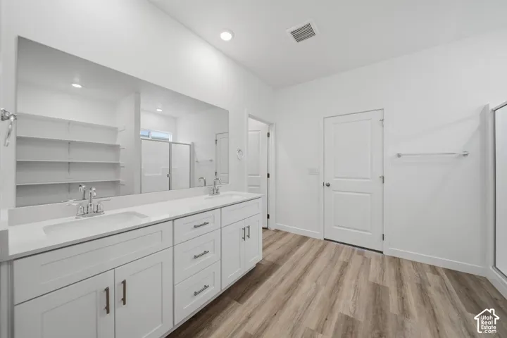 Dual vanity with white cabinetry, wood-finish flooring, recessed lighting, and a walk-in shower with clear glass enclosure