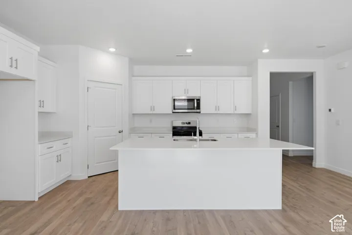 Kitchen featuring white cabinetry, light-colored countertops, stainless steel appliances, a center island, and wood-finish flooring