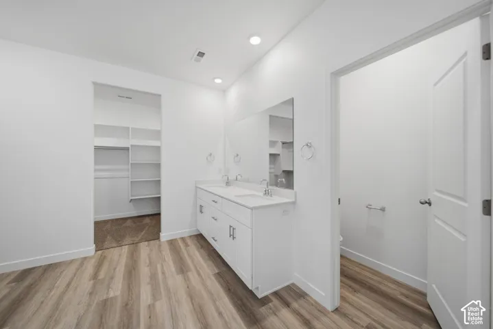 Wood-finish flooring, white double vanity with dual sinks, overhead recessed lighting, and a built-in closet system