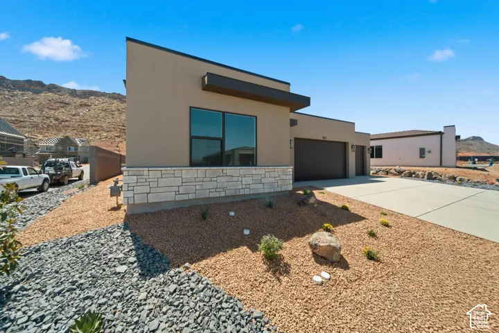 Contemporary exterior with stucco finish, stone veneer accenting, large windows, an integrated two-car garage, and desert landscaping