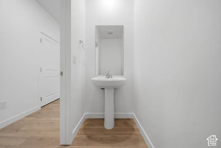 Pedestal sink with chrome faucet, wall-mounted mirror, wood-finish flooring, and white interior door
