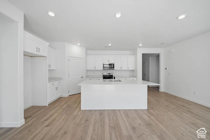 Kitchen featuring white cabinetry, integrated stainless steel appliances, a large center island, and wood-finish flooring