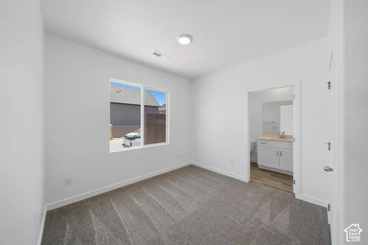 Recessed ceiling lighting, white walls, gray carpet, double-pane window, and an en-suite bathroom with a vanity and wood-finish flooring