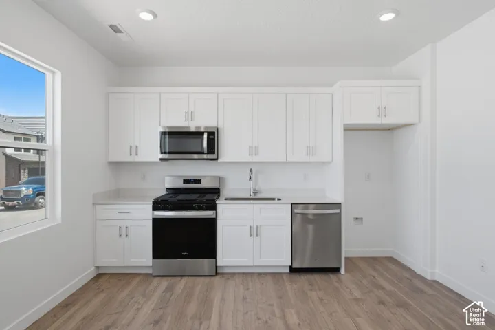 White shaker-style cabinetry, wood-finish flooring, recessed lighting, and stainless steel appliances