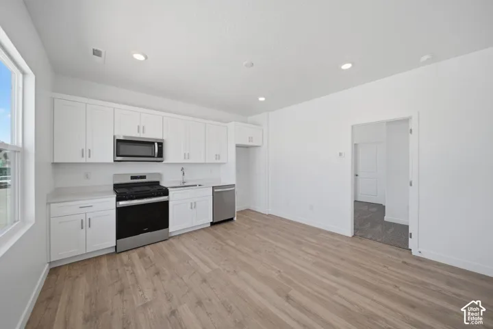 Kitchen featuring white shaker cabinetry, stainless steel appliances, light-toned countertops, and wood-finish flooring