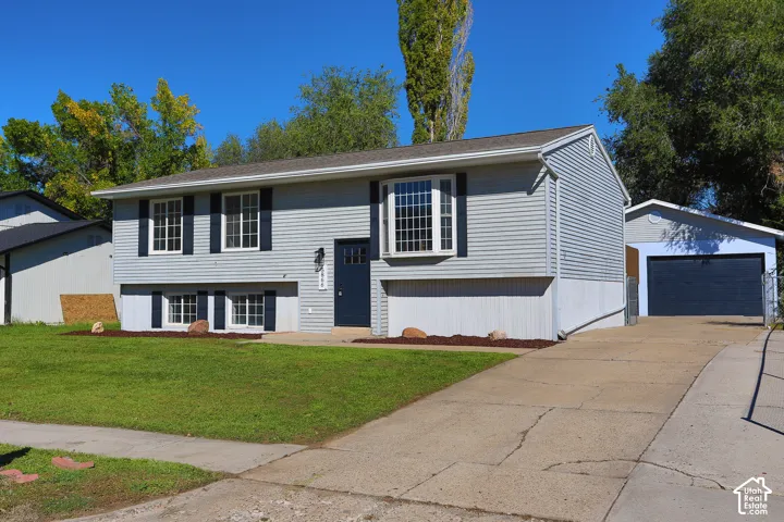 Split-level residence featuring light gray siding, dark shutters, and a bay window
