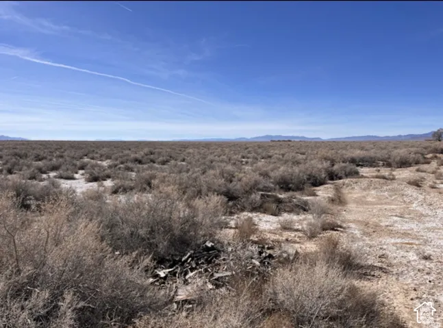 Expansive open land featuring natural desert vegetation, a clear blue sky, and distant mountain ranges