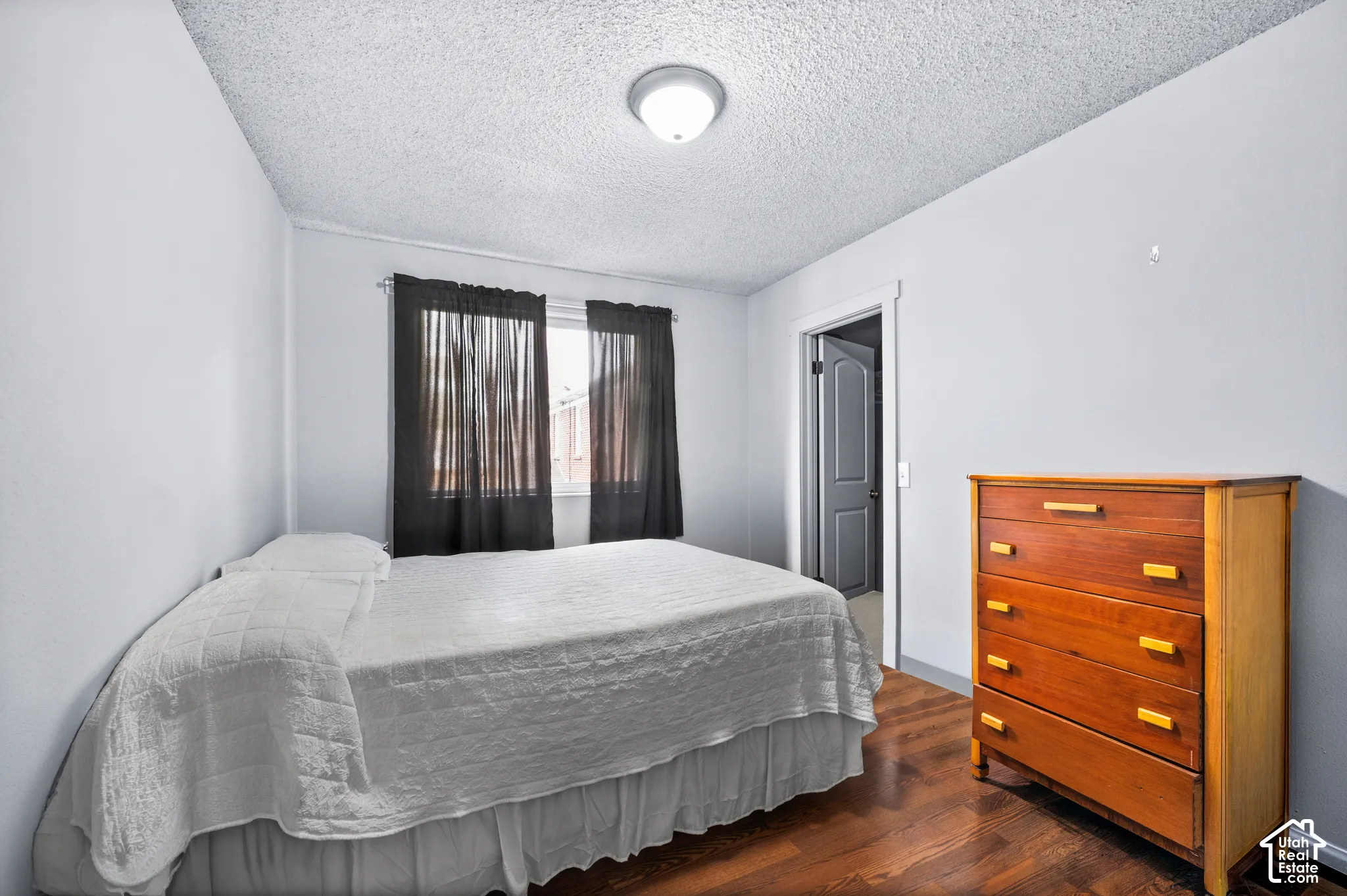 Wood-finish flooring with light-toned walls, featuring a window with dark drapery