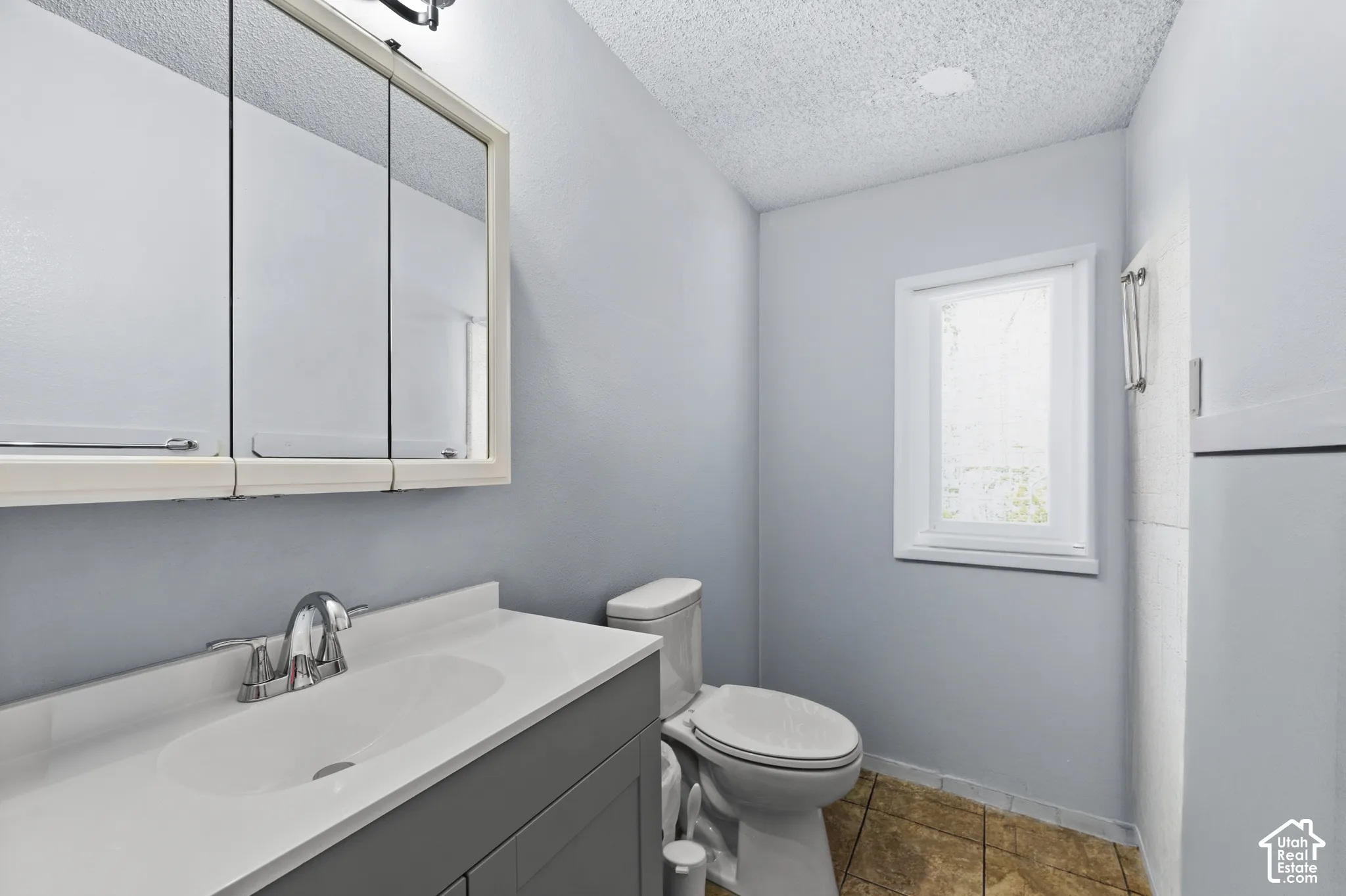 Bathroom featuring a single window, a vanity with an integrated sink, a mirrored medicine cabinet, and tiled flooring