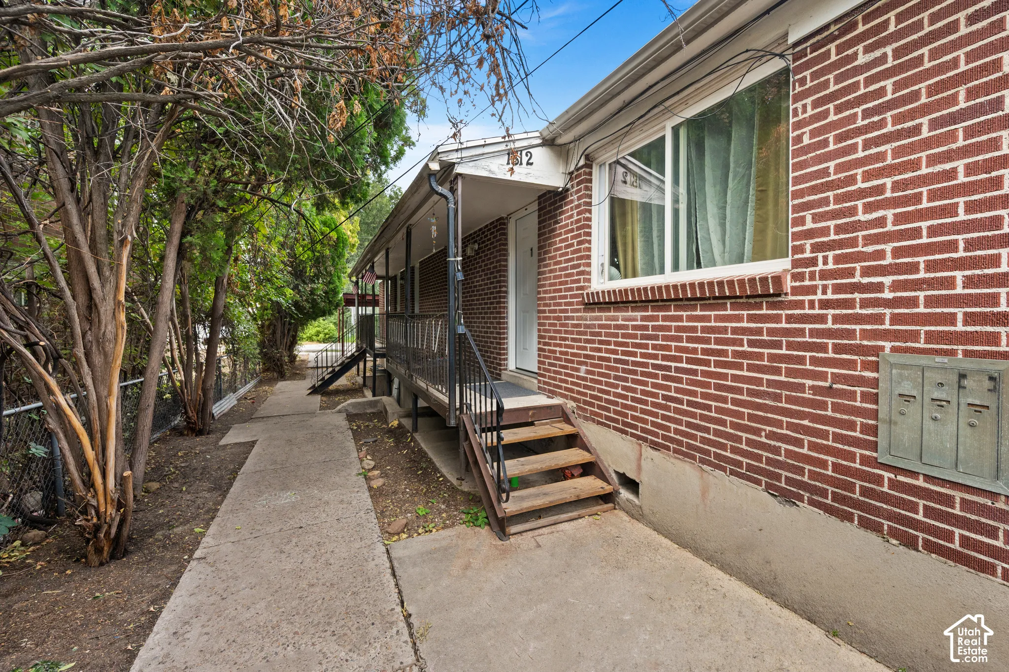 Red brick exterior with white window trim, featuring a covered entryway with black railings