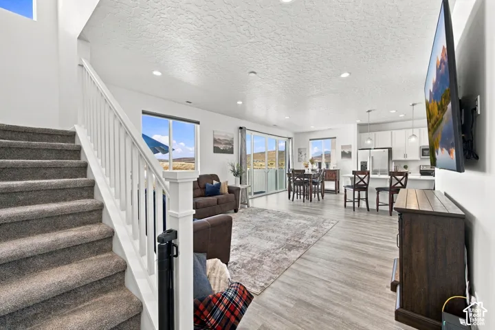 Expansive open-concept living space with wood-finish flooring, recessed lighting, and a white staircase with carpeted treads