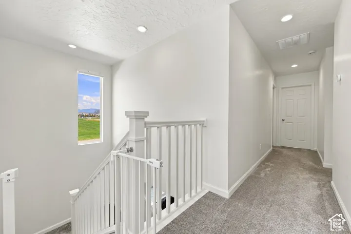 Recessed ceiling lighting, white painted balusters, a rectangular window, and light grey carpeting throughout