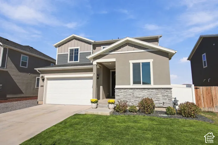 Modern exterior featuring a stucco and stone facade, contrasting siding, an attached garage, a concrete driveway, and a manicured lawn