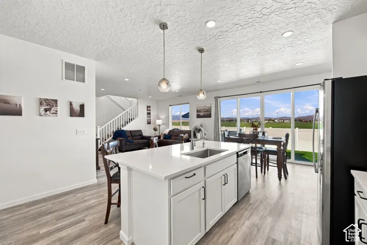 Kitchen island with white cabinetry, stainless steel sink, and pendant lighting