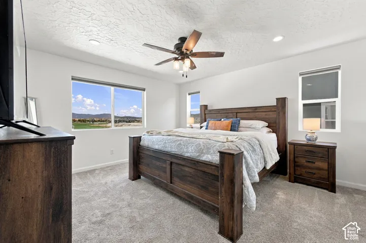 Primary bedroom. Light-toned carpeting, white walls, and a ceiling fan with integrated lighting