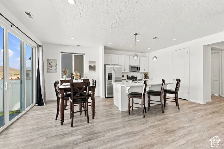 Open-concept living space featuring wood-finish flooring, white cabinetry, stainless steel appliances, and a kitchen island with pendant lighting