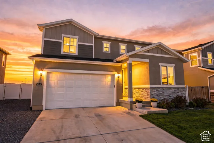 Two-story exterior featuring a stone and stucco facade, a two-car garage, a concrete driveway, a covered front entry, and a manicured lawn