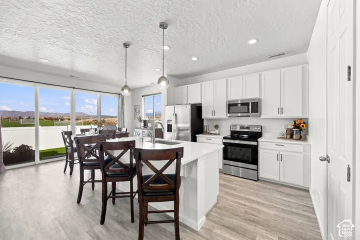 Kitchen featuring a central island with bar seating, pendant lighting, stainless steel appliances, white cabinetry, and wood-finish flooring
